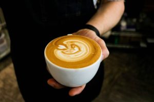 Eine Tasse mit Cappuccino in der Hand
